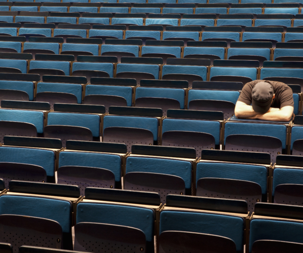 A man sitting in an auditorium with his head resting in his arms