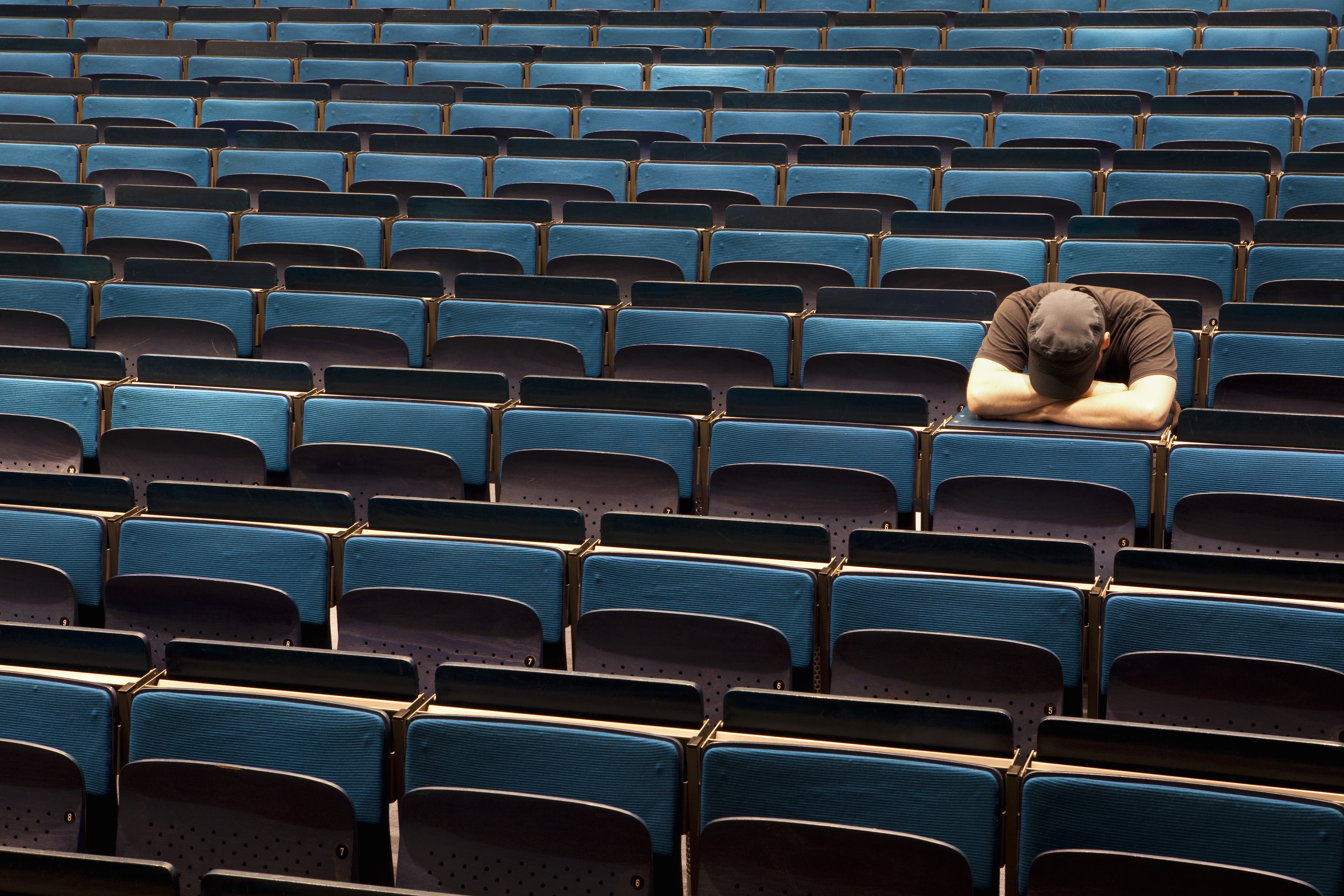 A man sitting in an auditorium with his head resting in his arms